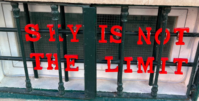 pic of basement window with sign behind iron bars reading 'Sky is Not the Limit' in red letters