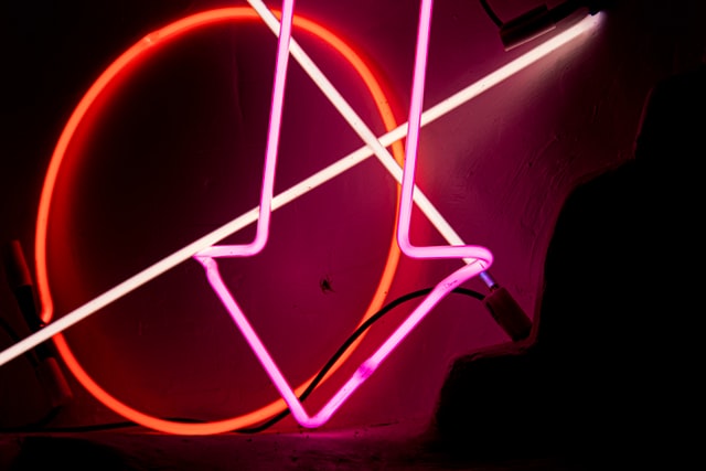 pic of white neon lights crisscrossing glowing red circle overlaid by hot pink down pointing arrow