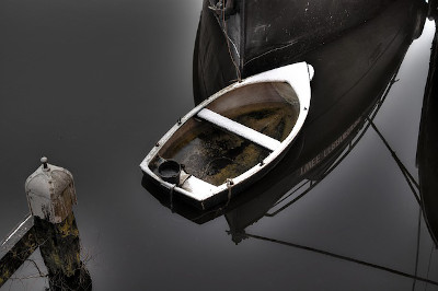 pic of skiff on lake in shadows of a larger vessle